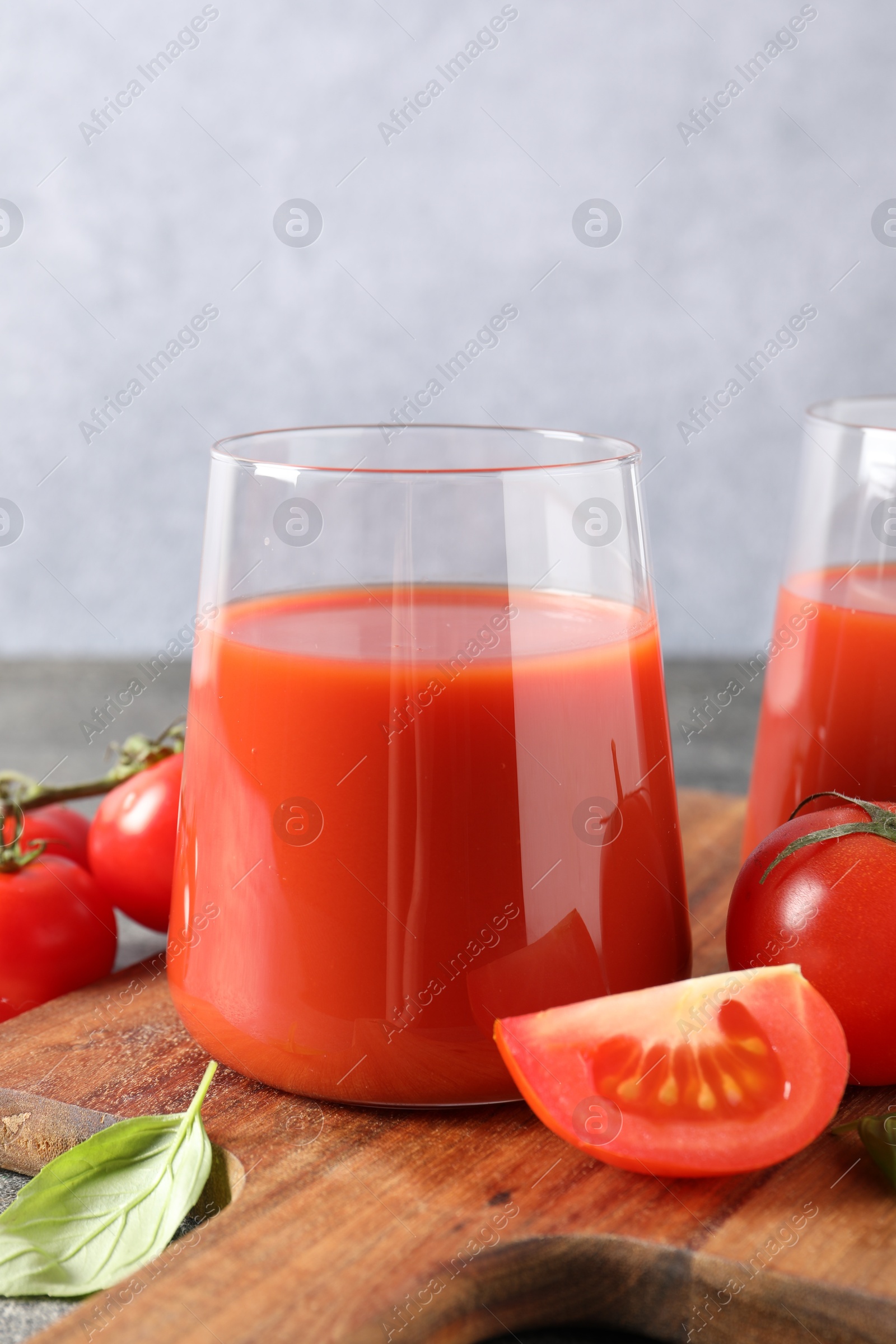 Photo of Tasty tomato juice in glass, basil and fresh vegetables on table