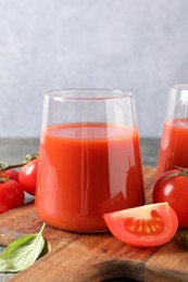 Tasty tomato juice in glass, basil and fresh vegetables on table