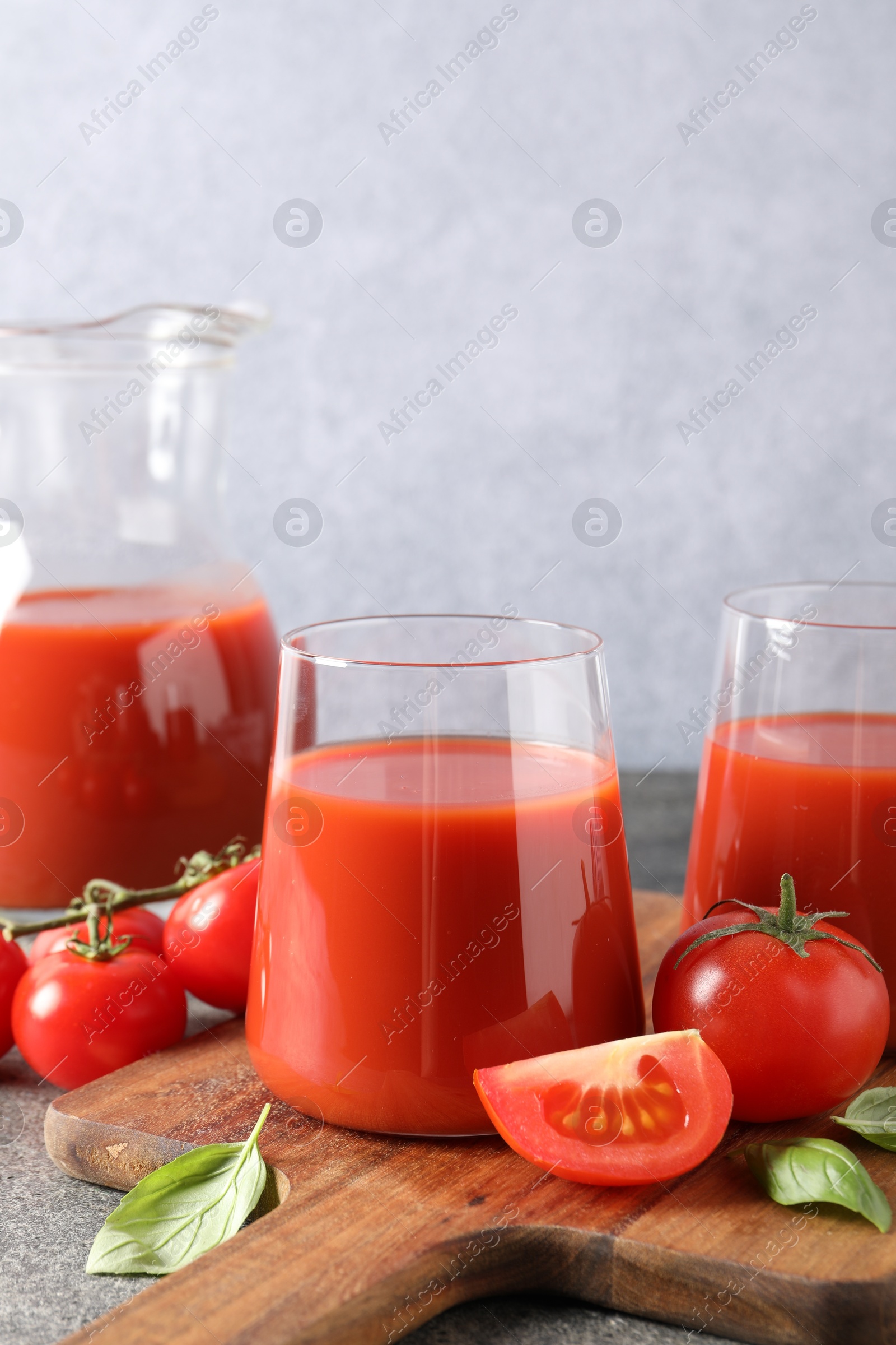 Photo of Tasty tomato juice in glasses, basil and fresh vegetables on grey table