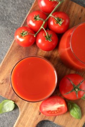 Tasty tomato juice in glasses, basil and fresh vegetables on grey table, top view