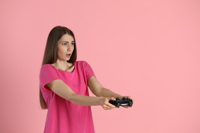 Woman playing video games with controller on pink background, space for text