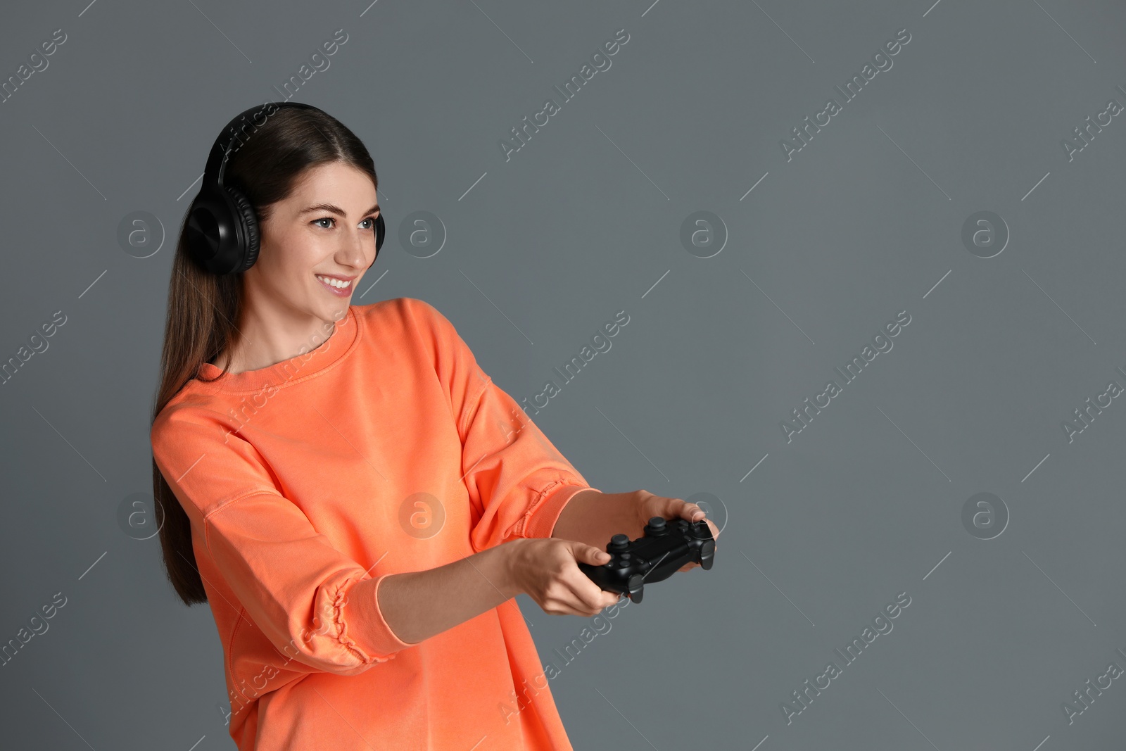 Photo of Happy woman in headphones playing video games with controller on gray background, space for text