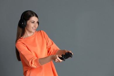 Happy woman in headphones playing video games with controller on gray background, space for text