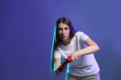 Surprised woman playing video games with controller on violet background, space for text