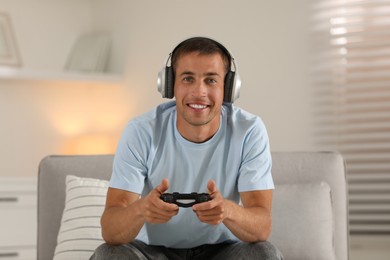 Photo of Happy man in headphones playing video games with joystick at home