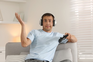 Emotional man in headphones playing video games with joystick at home