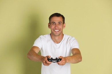 Happy man playing video games with controller on light green background