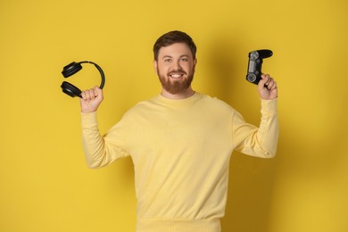 Photo of Happy man with game controller and headphones on pale yellow background