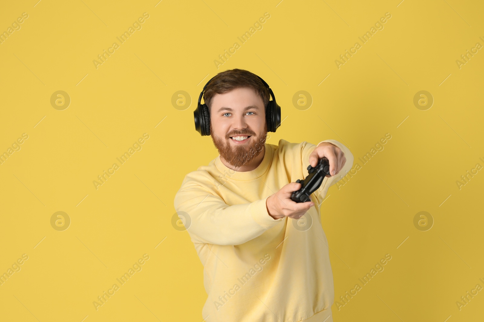 Photo of Happy man in headphones playing video game with controller on pale yellow background