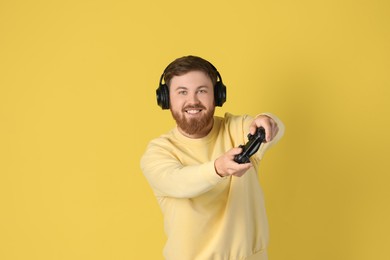 Photo of Happy man in headphones playing video game with controller on pale yellow background