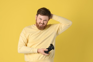 Emotional man with game controller on pale yellow background
