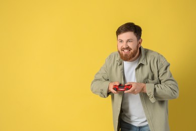 Photo of Happy man playing video game with controller on pale yellow background. Space for text