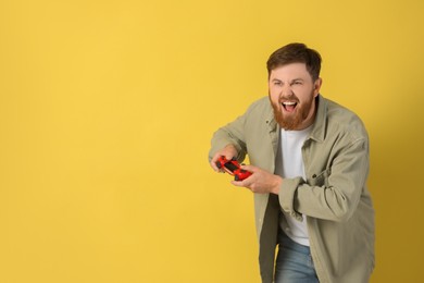 Photo of Emotional man playing video game with controller on pale yellow background. Space for text