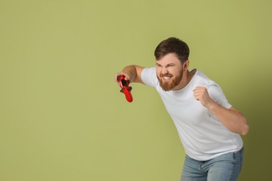 Emotional man with game controller on pale green background. Space for text