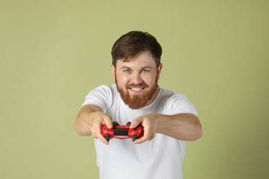 Happy man playing video game with controller on pale green background