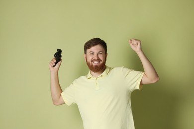 Happy man with game controller on pale green background