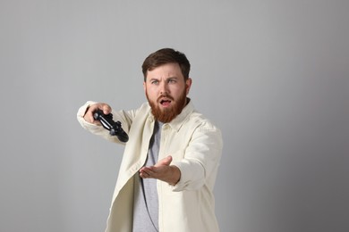 Surprised man with game controller on grey background