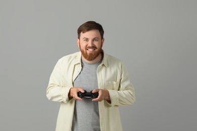 Happy man playing video game with controller on grey background