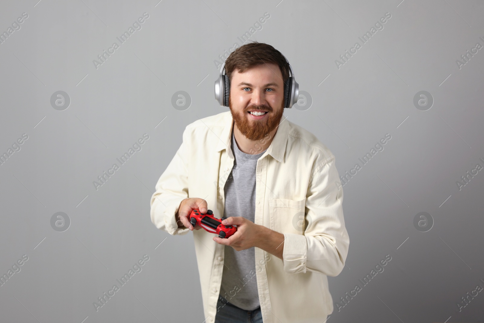 Photo of Happy man in headphones playing video game with controller on grey background