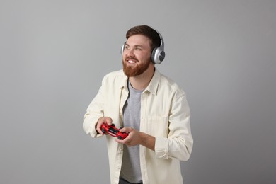 Photo of Happy man in headphones playing video game with controller on grey background