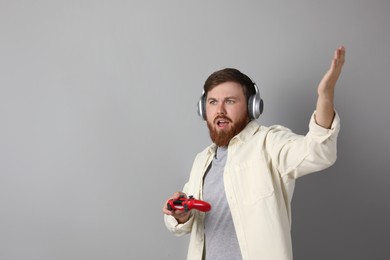 Emotional man in headphones with game controller on grey background. Space for text