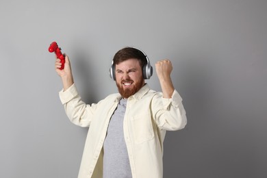 Emotional man in headphones with game controller on grey background