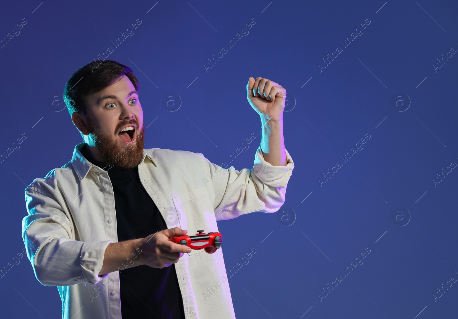 Photo of Emotional man with game controller on dark blue background. Space for text