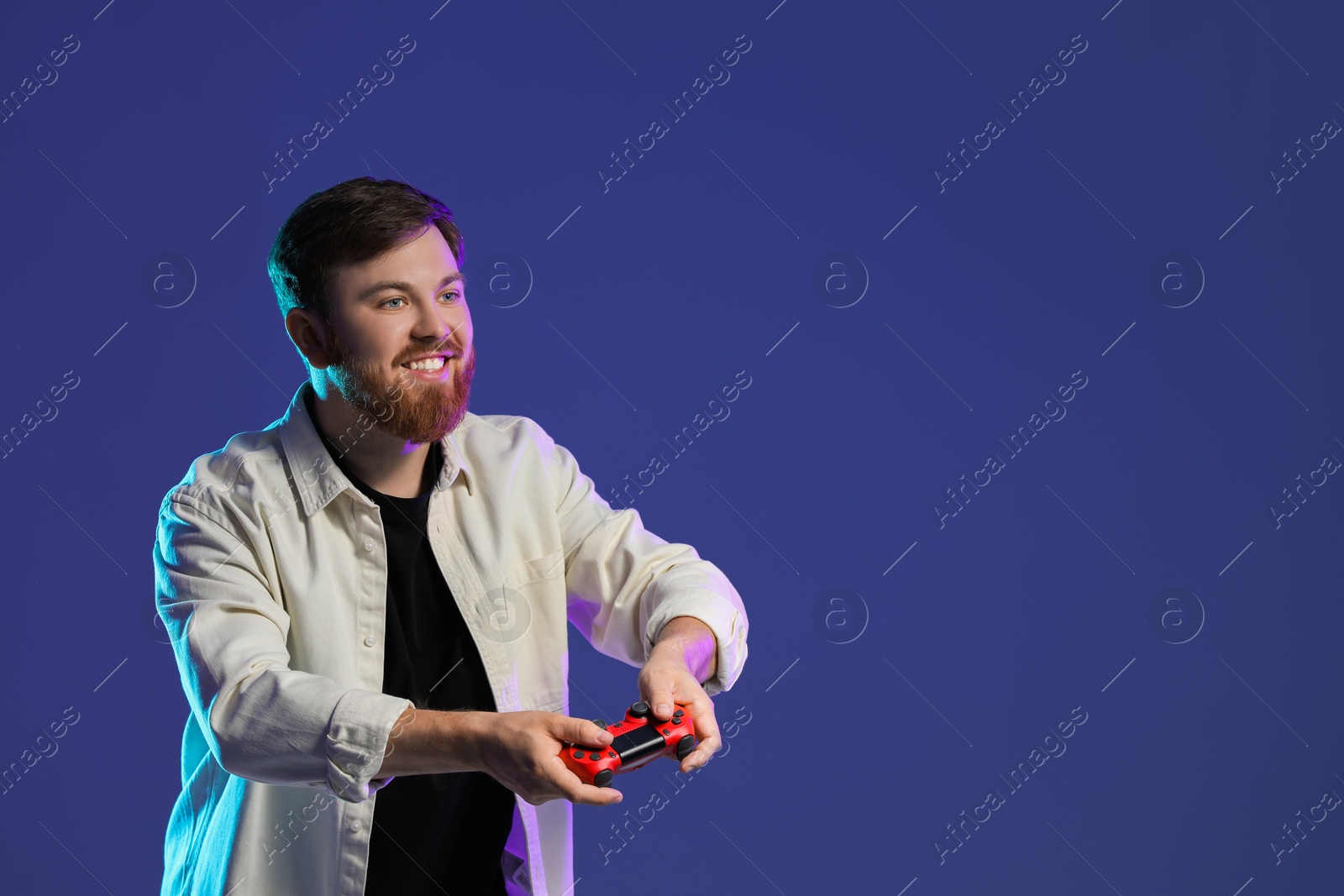 Photo of Happy man playing video game with controller on dark blue background. Space for text