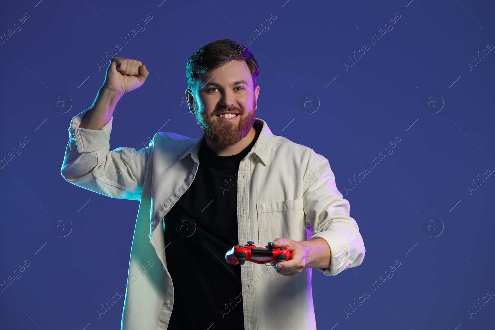 Photo of Happy man with game controller on dark blue background