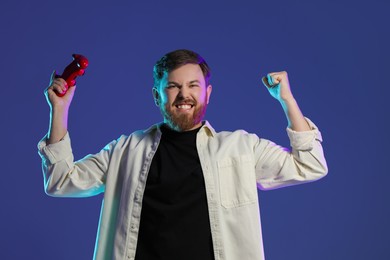 Emotional man with game controller on dark blue background