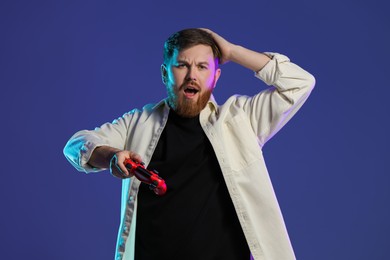 Emotional man with game controller on dark blue background