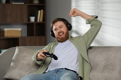 Photo of Happy man in headphones with game controller at home