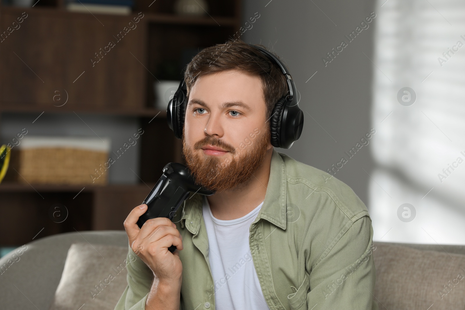 Photo of Young man in headphones with game controller at home