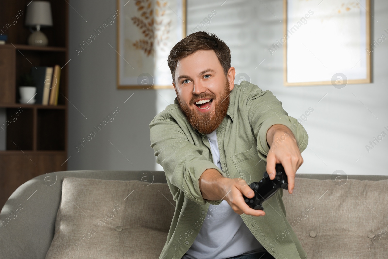 Photo of Happy man playing video game with controller at home