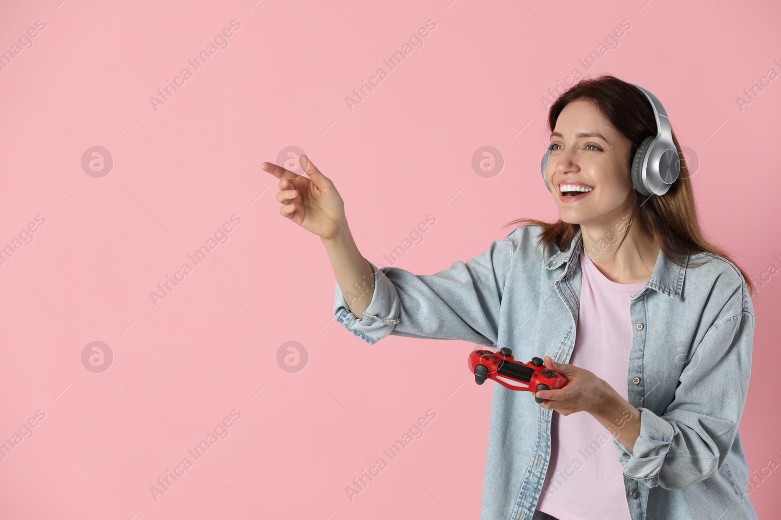 Photo of Happy woman in headphones with game controller on pink background. Space for text