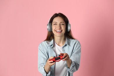 Happy woman in headphones with game controller on pink background