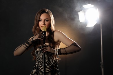 Beautiful young woman with microphone singing on dark background with smoke