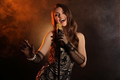 Beautiful young woman with microphone singing in color lights and smoke