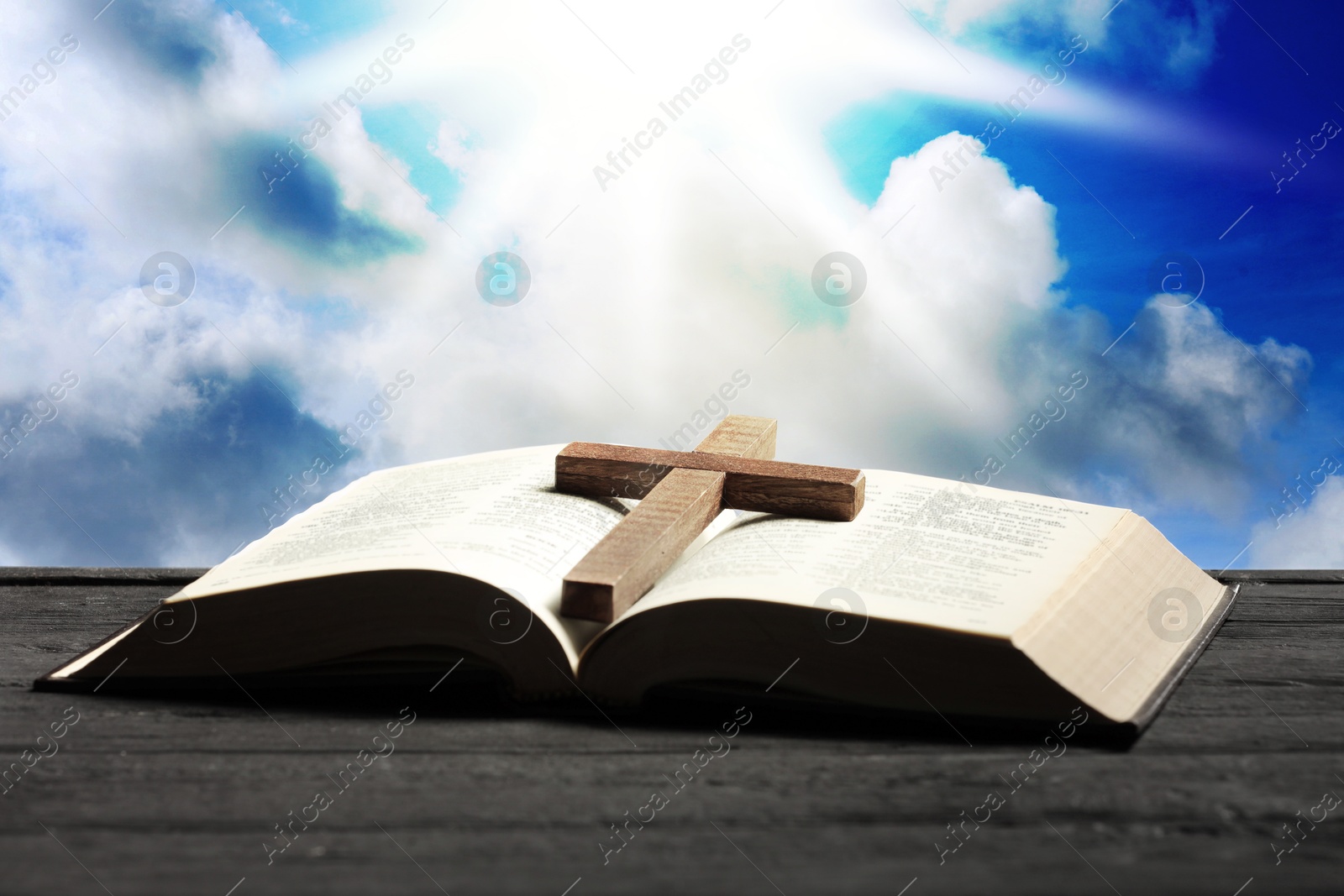 Image of Holy Bible with cross on wooden table against blue sky. Religion of Christianity