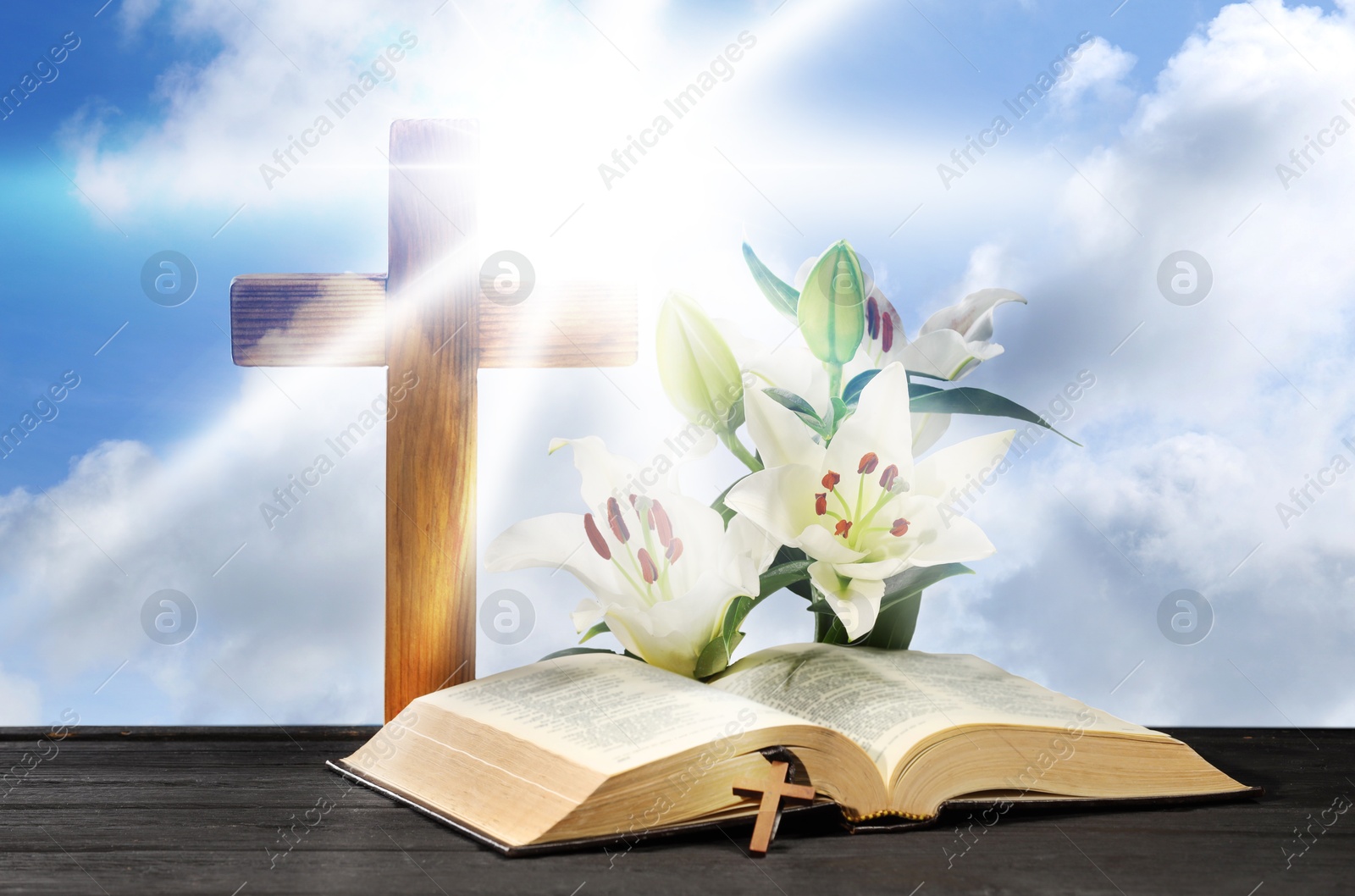 Image of Holy Bible, cross and lily flowers on wooden table against blue sky. Religion of Christianity