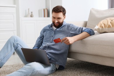 Online banking. Happy young man with credit card and laptop paying purchase at home