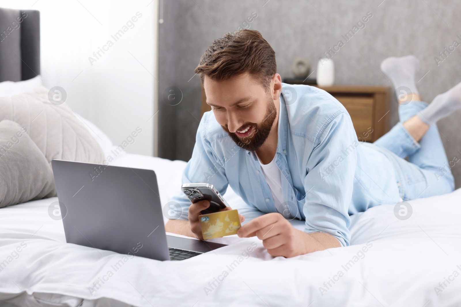 Photo of Online banking. Happy young man with credit card and laptop paying purchase at home