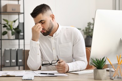 Overwhelmed man with glasses sitting at table in office