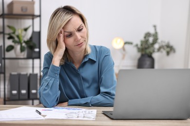 Photo of Overwhelmed woman sitting at table with laptop and documents in office