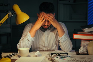 Photo of Overwhelmed man at workplace in office at night
