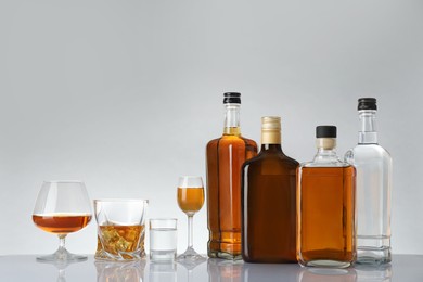 Bottles and glasses with different alcoholic drinks on white table against light background