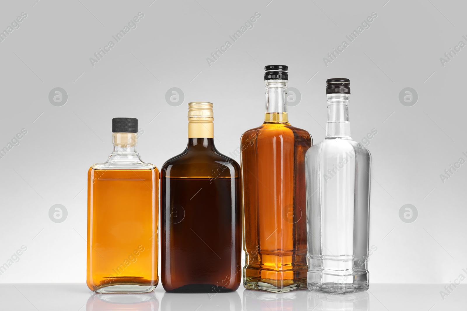 Photo of Bottles of different alcoholic drinks on white table against light background