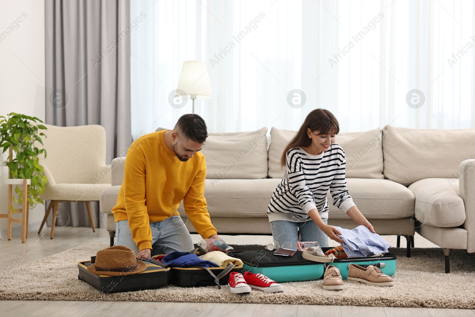 Photo of Couple packing suitcases for trip on floor at home