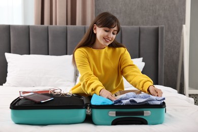 Photo of Woman packing suitcase for trip on bed indoors
