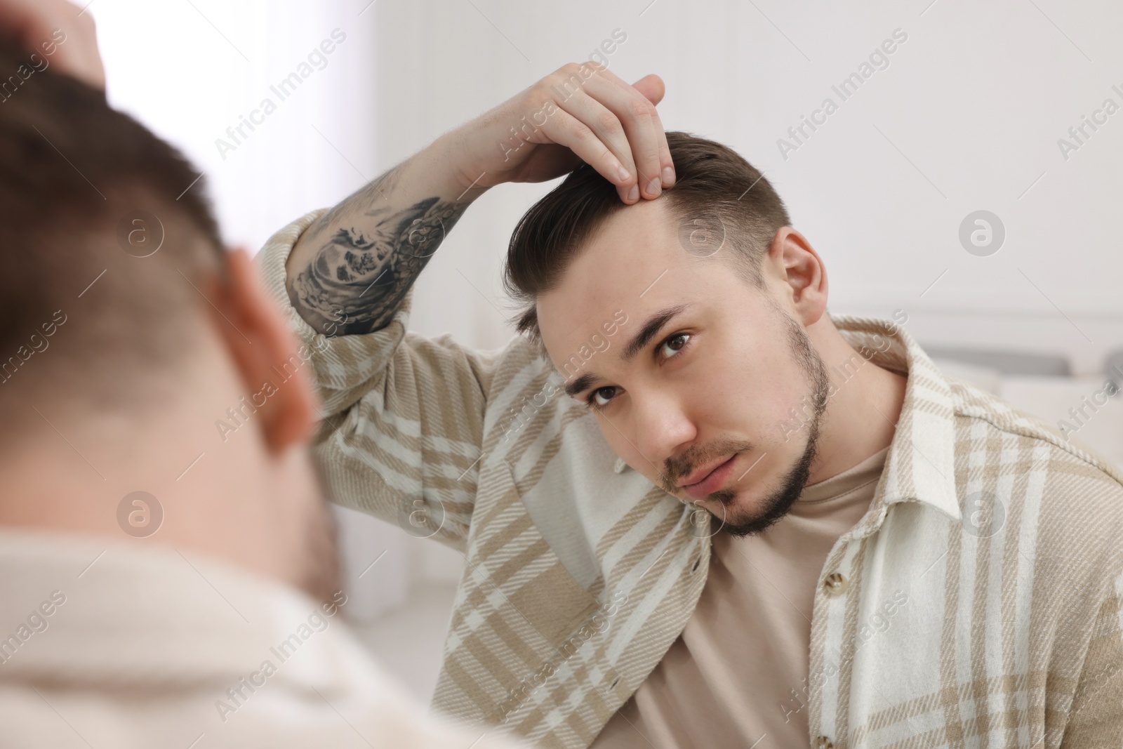 Photo of Baldness concept. Sad man with receding hairline looking at mirror indoors